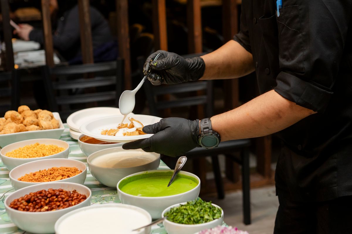 Chef preparing Indian street food chaat with fresh toppings and spices